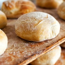 Freshly baked round loaves of white bread straight from the oven on wooden shelves or tables in a bakery